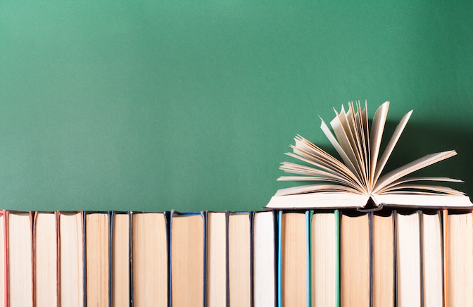 books lined up agains a green wall with one book resting on top of the rest open