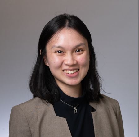 Shows Nina Ye, who has shoulder length black hair and is wearing a brown jacket and black shirt