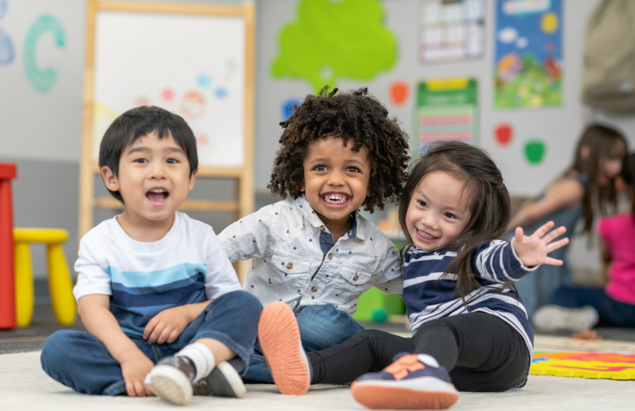 Three preschool ages children sitting in classroom smiling at camera