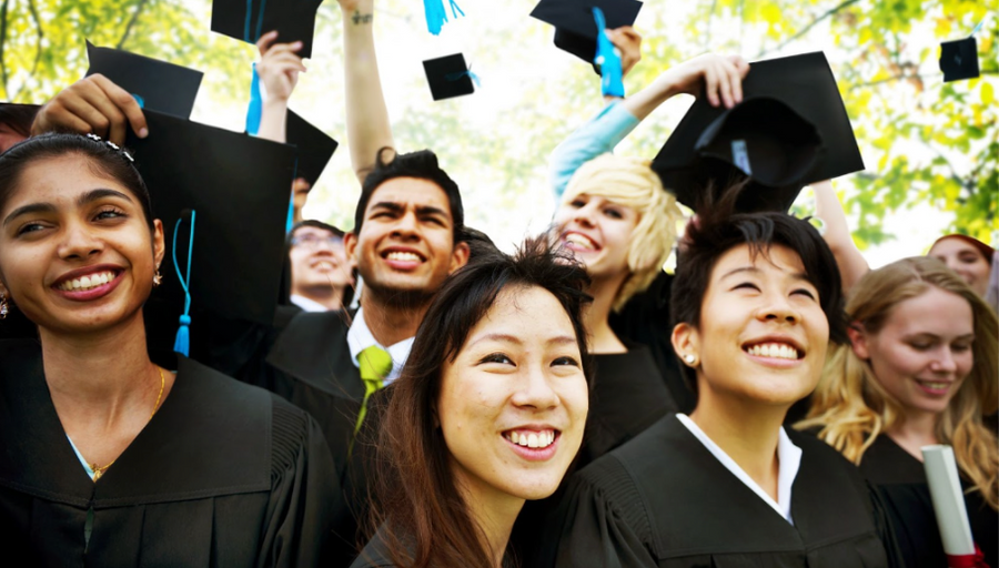 graduates in black caps a gowns smiling at the camera while throwing their hats