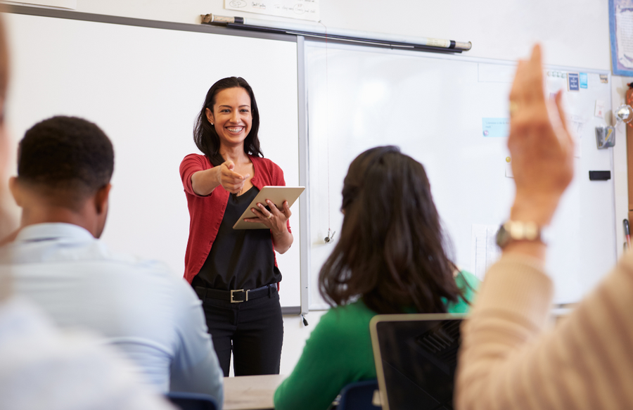 Female teacher speaking to a class of their peers with one hand raised as she is speaking