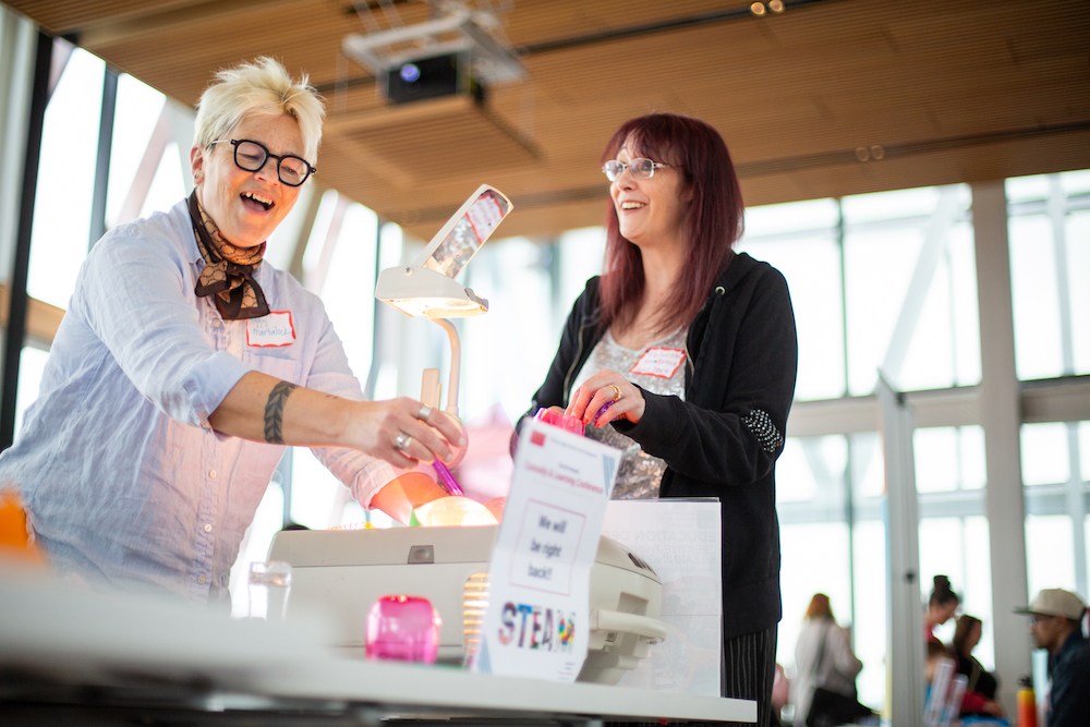 two female participants around a table smiling at the 2024 Curiosity and Learning Conference