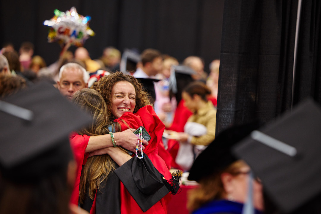 Women embracing another women in a graduation robe smiling