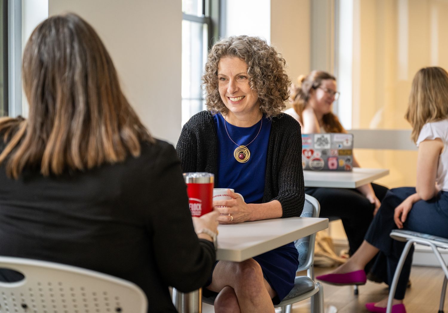 Penny Bishop sits at table smiling talking with Elizabeth Vassallo