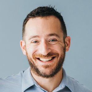 Shows head and shoulders of Benjamin Feit, who has short hair and a beard and is wearing a blue collared shirt