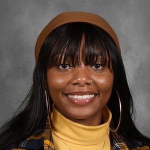 Shows Jacqueline Ferguson, who has long black hair and is wearing a yellow turtleneck and plaid shirt
