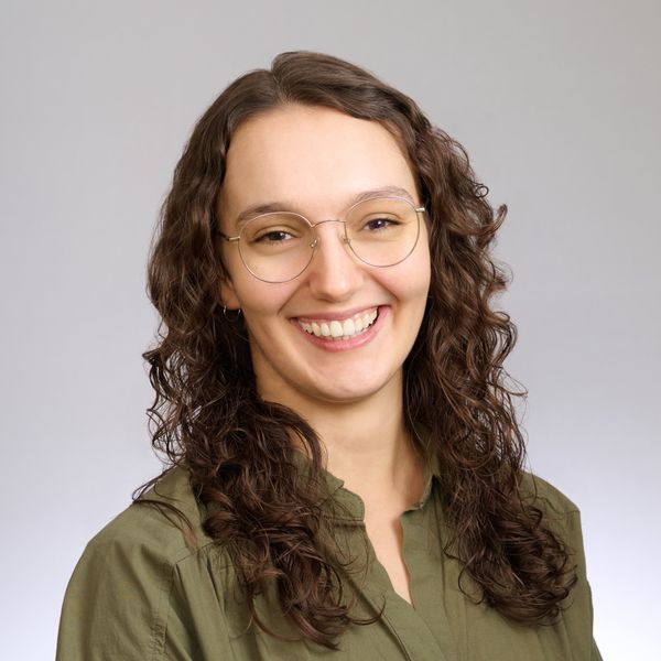 Shows Paris Gappmayr, who has long brown hair and is wearing glasses and an olive green collared shirt