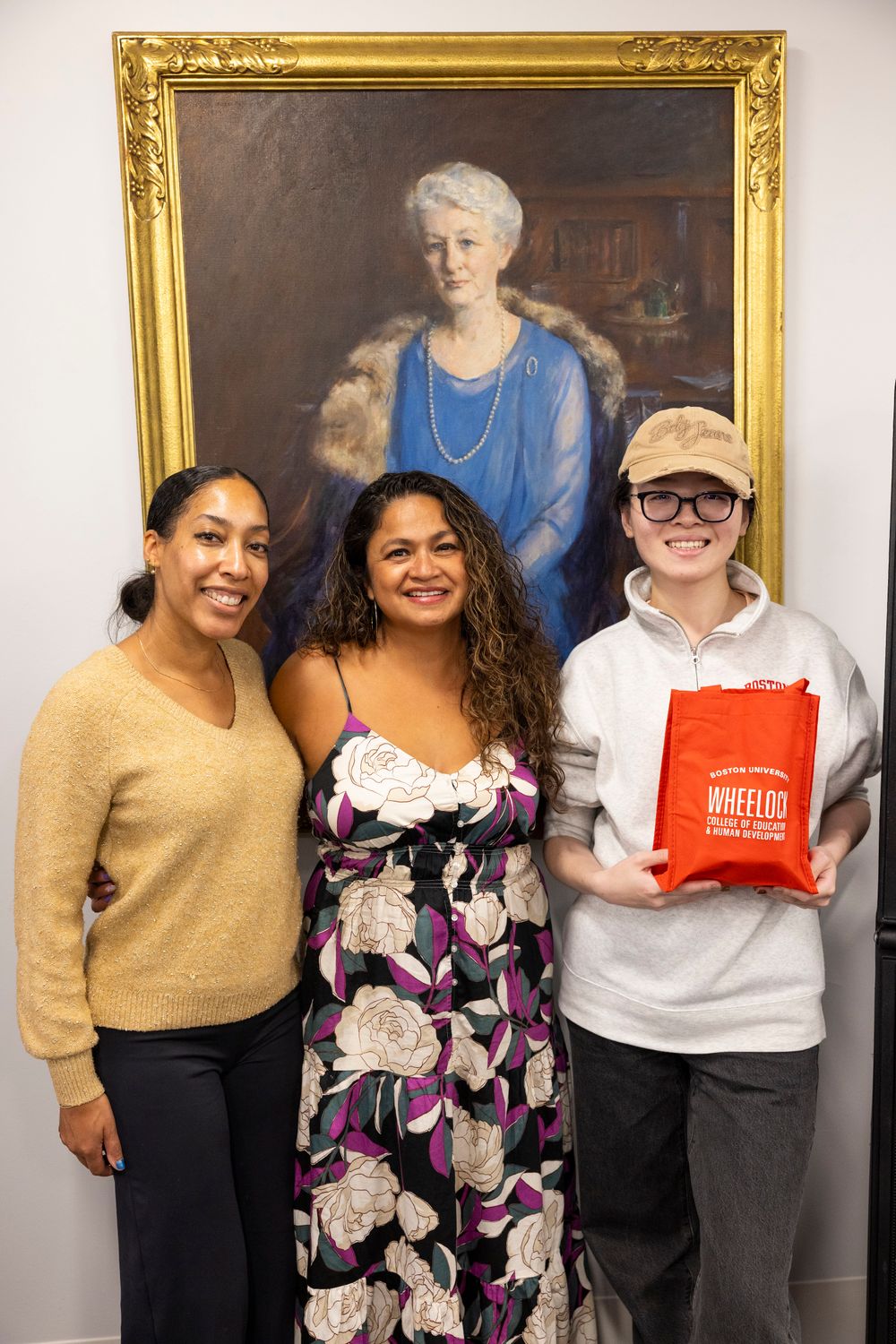 Three alums smiling infront of Lucy Wheelock portrait