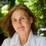 Deb Buehler stands smiling in a white button down leaning on a wooden beam