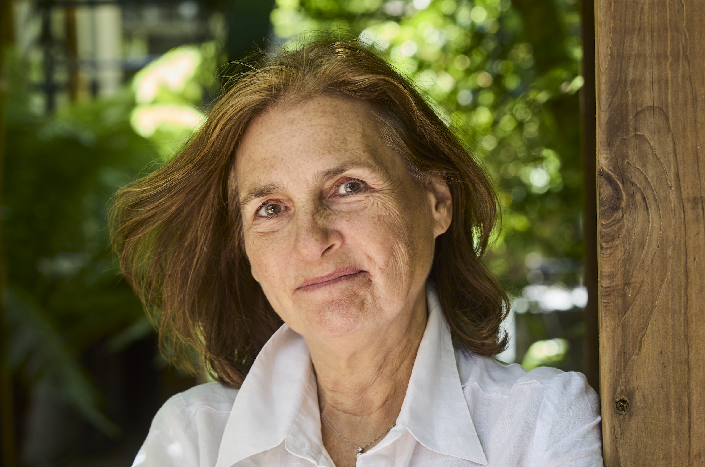 Deb Buehler stands smiling in a white button down leaning on a wooden beam
