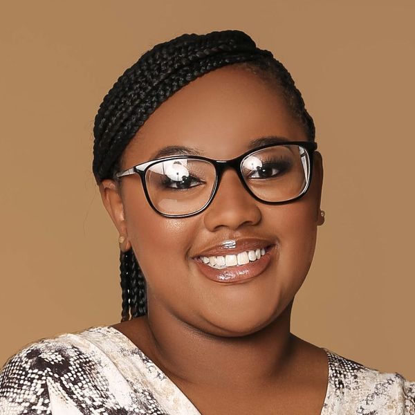 Shows Knadja Sims who has dark braided hair and is wearing glasses and a white and black shirt