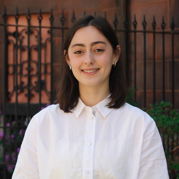 Headshot of Dommie Bochman in a white button down shirt smiling infront of stone building