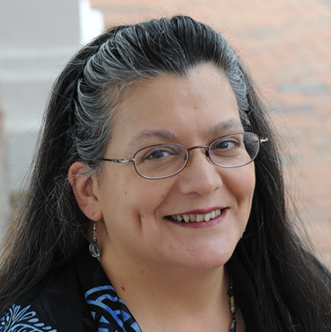 Deborah Miranda smiling at the camera in a patterned blue sweater