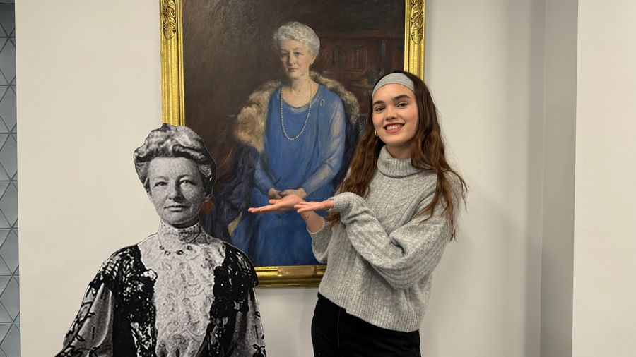Female student smiling with black and white cutout of Lucy Wheelock infront of a portrait of Lucy Wheelock