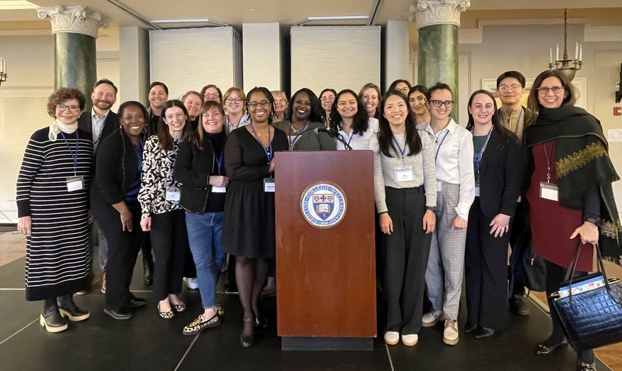 A group of faculty, staff, and students standing around a lectern with a Massachusetts state seal on it.