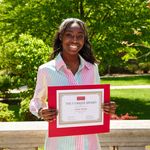 Shows woman standing outside holding an award certificate