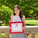 Shows woman standing outside holding award certificate