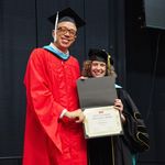 Shows a man in a red graduation robe standing next to the dean