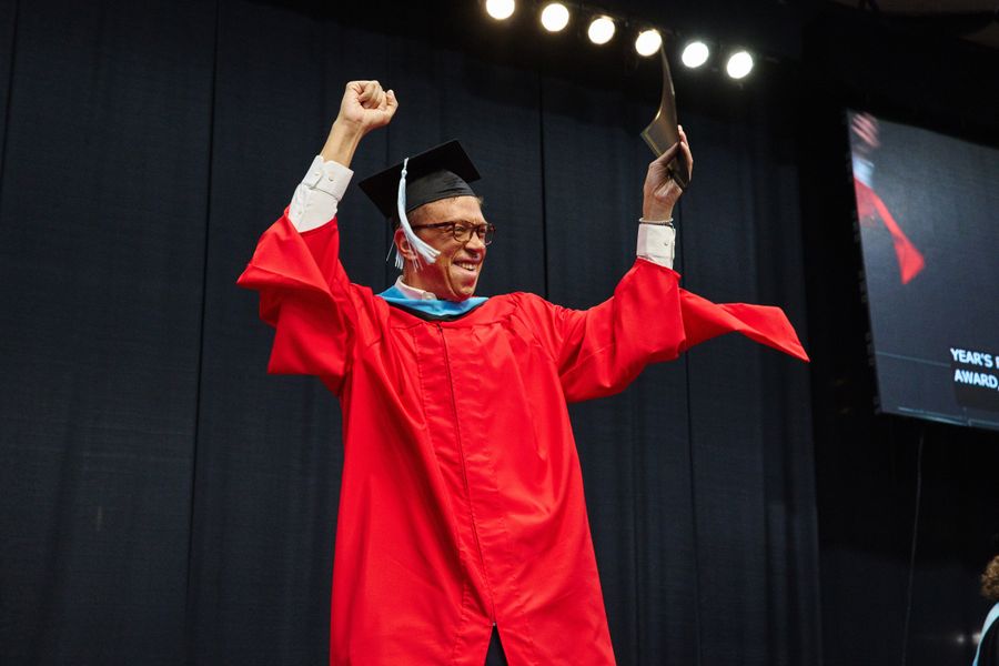 Shows man in red graduation robes cheering with raised arms