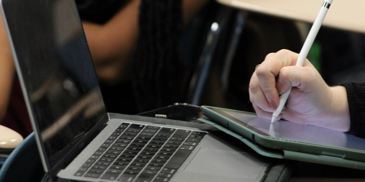 A laptop and a hand writing on a notebook