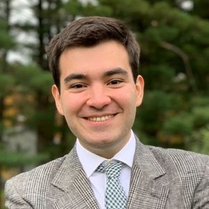 Shows Ignacio Chaparro, who has short brown hair and is wearing a plaid jacket, white shirt, and green and white tie