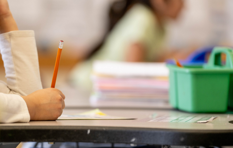 Shows a child's hand writing with a pencil at a desk