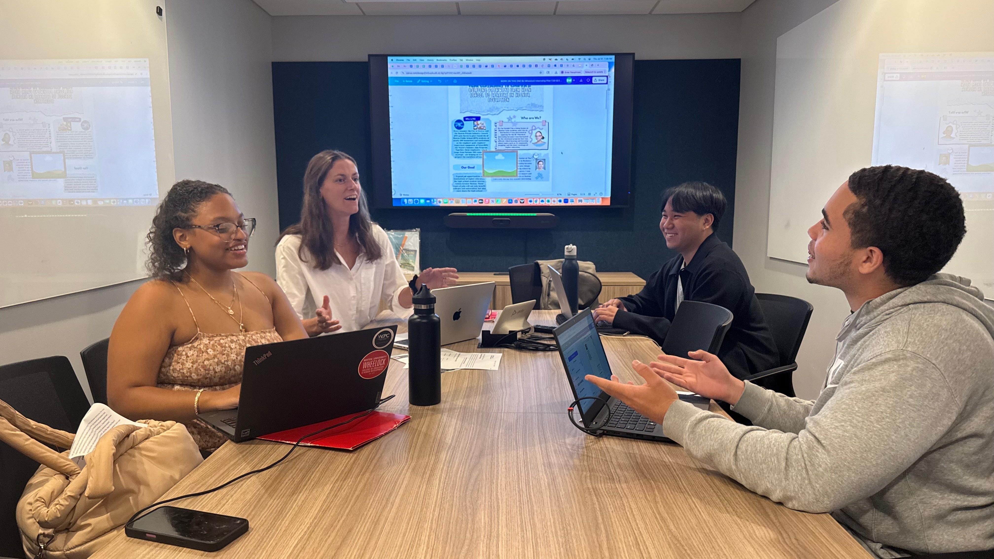 Four people in a conference room in front of a large screen