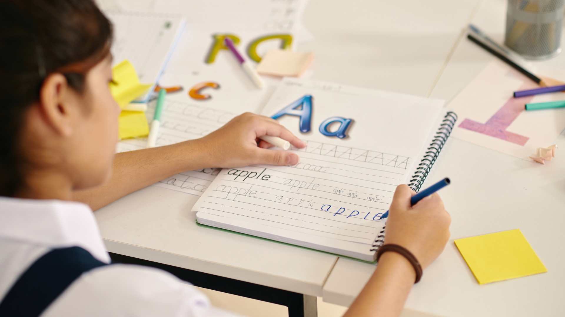 A girl sits at a desk writing in a lined notebook