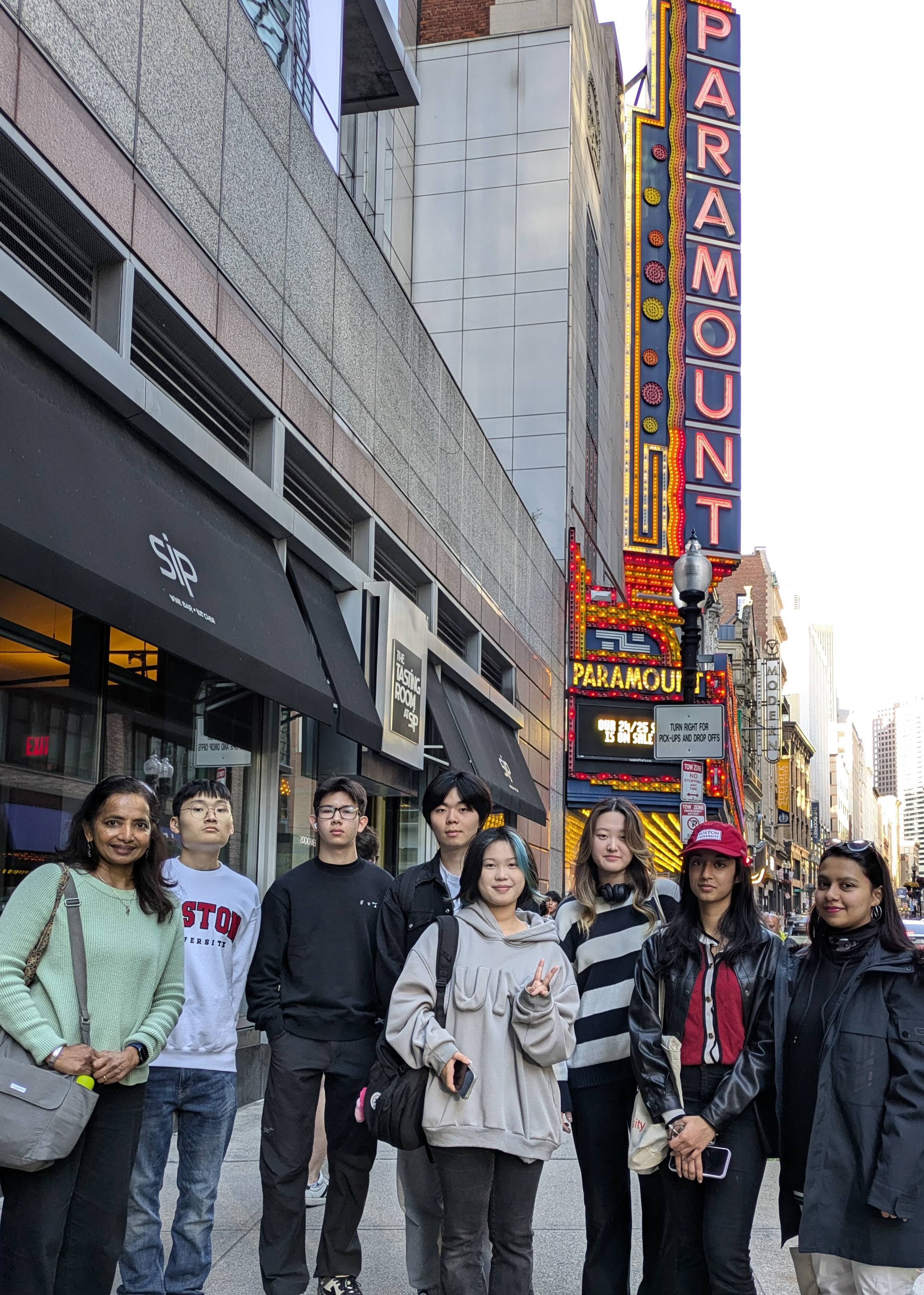 Seven international students plus one Writing Program faculty member stand on the sidewalk in downtown Boston in front of the Paramount theatre