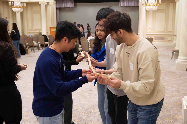 Students using wooden sticks, building a bridge for marble.