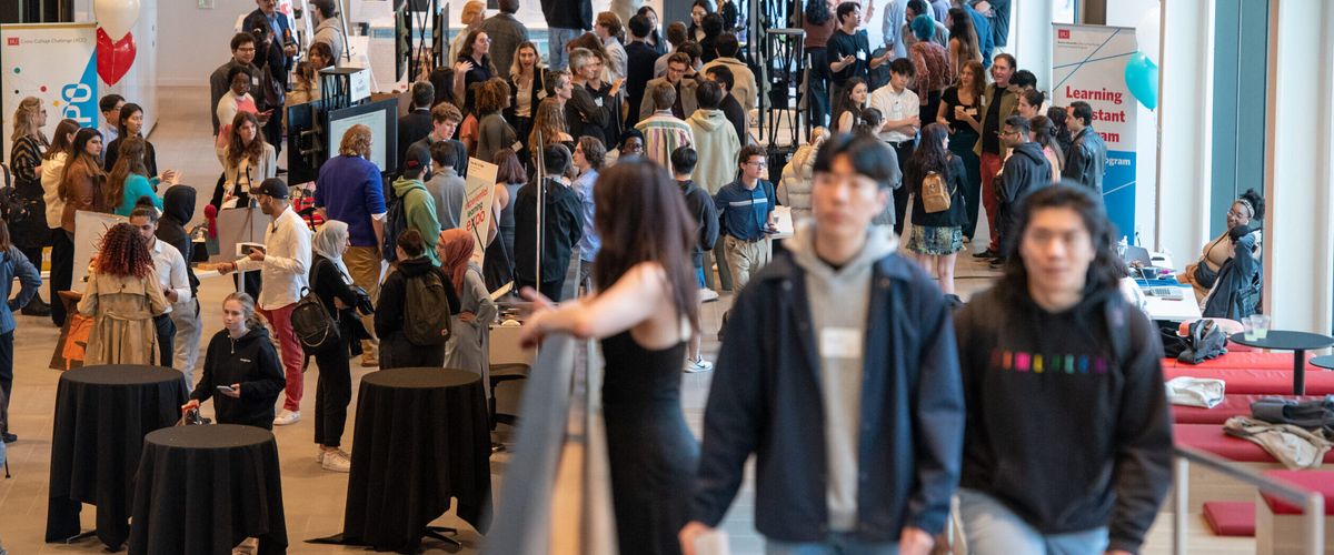 In an overcrowded room, students present projects while others mingle around.