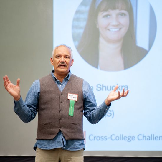 A faculty member stands before students, talking and raising his hands.