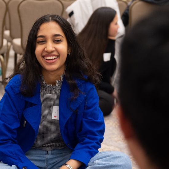 A student sits on the floor, smiling.